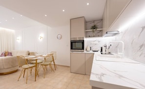 A modern kitchen with a built-in oven, microwave, and sink. There is a dining area with a table and chairs. - Les Maisons Deluxe Superior by RentalsPro (Afitos)