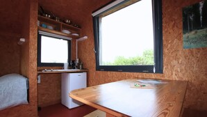 Een compacte keuken met een houten tafel, een kleine koelkast en een raam met uitzicht op groen.