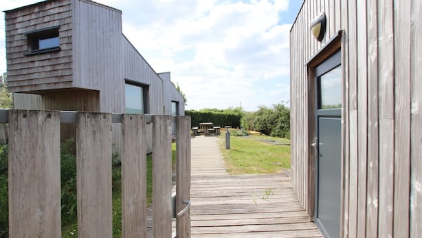 Een houten terras dat leidt naar een modern gebouw met een deur en een raam.