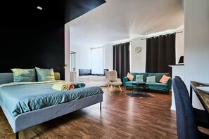 A modern hotel room with a large bed, a sofa, a chair, and a small table. - Grand Studio Avec Balneo Proche Gare (Tourcoing)