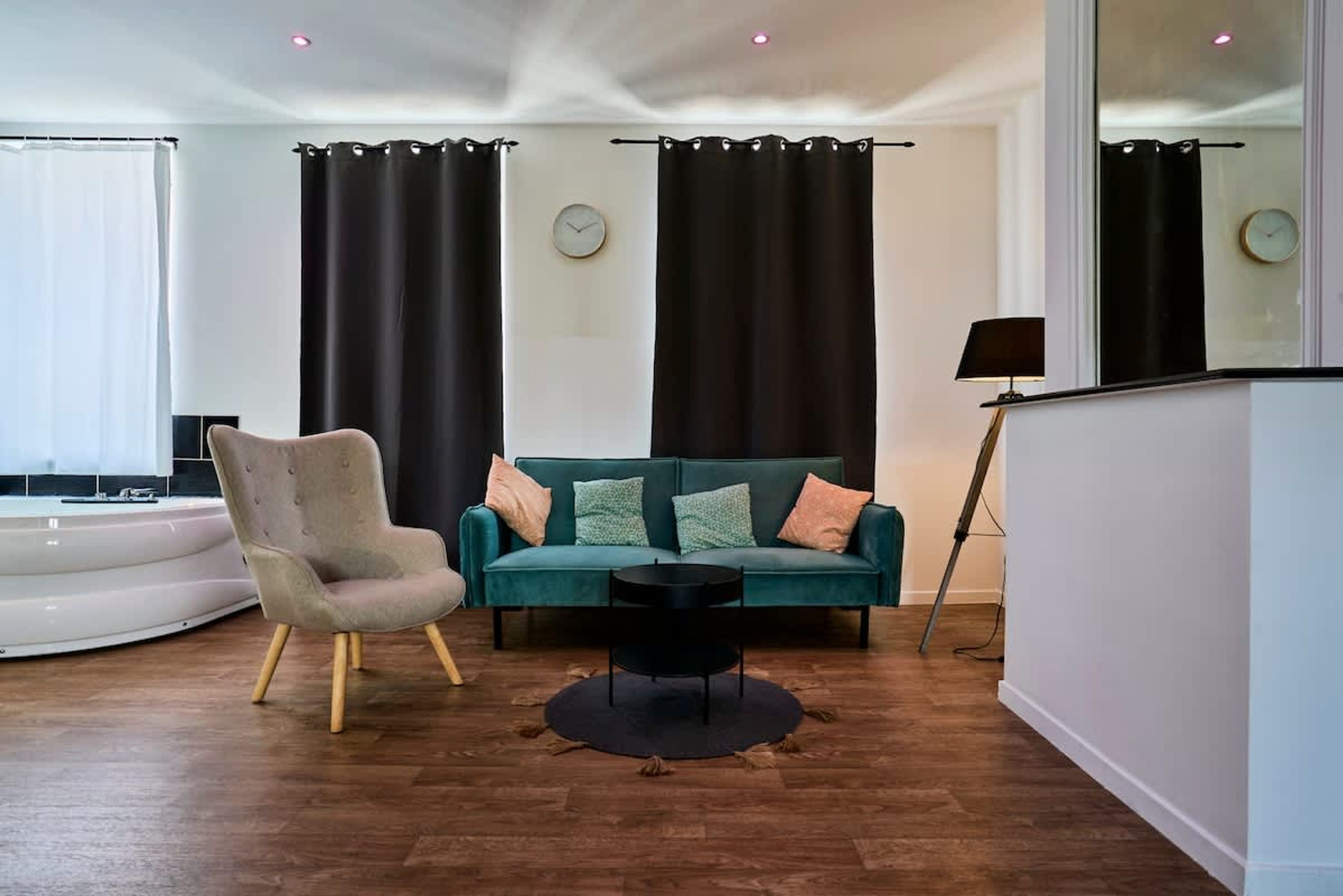 Una sala de estar moderna con un sofá verde azulado, un sillón gris, una mesa de centro negra y un espejo grande.