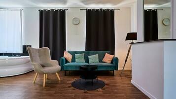 Una sala de estar moderna con un sofá verde azulado, un sillón gris, una mesa de centro negra y un espejo grande.