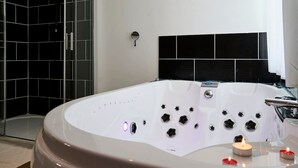 A modern bathroom with a large white bathtub, a shower enclosure, and a black tiled wall. - Grand Studio Avec Balneo Proche Gare (Tourcoing)