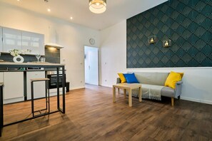 Moderni keittiö, jossa on ruokailutila, tyynyillä varustettu sohva ja kuvioitu seinä.