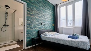 Un dormitorio con cama, mesita de noche, ducha, ventana y pared con diseño ondulado.