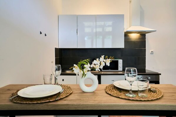 Une cuisine moderne avec des meubles blancs, un four à micro-ondes et une table à manger dressée avec des assiettes et des verres.
