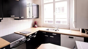 A modern kitchen with black cabinets, a built-in oven, a coffee maker, and a window providing natural light. - Le Voyageur Gare de Lens Wifi 4 Pers (Lens)