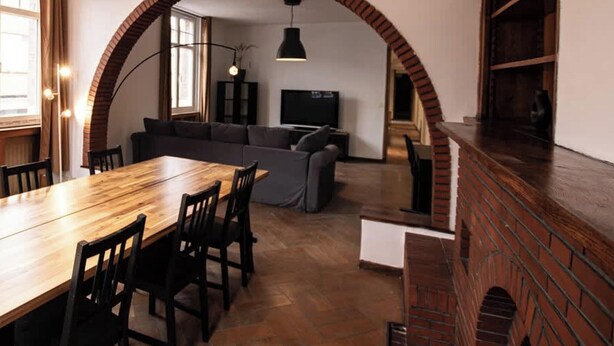 A dining area with a wooden table and chairs, a brick fireplace, and a living room with a sofa and television. - Le Voyageur Gare de Lens Wifi 4 Pers (Lens)