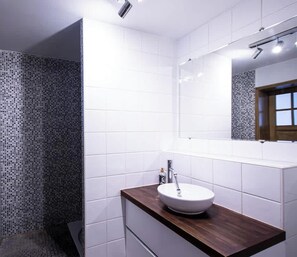Ein Badezimmer mit weißen Fliesen, einem Holzwaschtisch, einem weißen Waschbecken und einer Dusche mit gemusterten Fliesen.