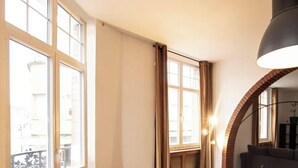 A room with large windows, a curved brick wall, a dark sofa, and a modern pendant light. - Le Voyageur Gare de Lens Wifi 4 Pers (Lens)