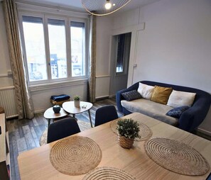 Een moderne woonkamer met een bank, een eettafel met placematen en een stadszicht door grote ramen.