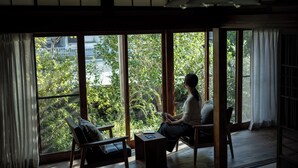 Ein Zimmer mit großen Fenstern, Holzboden und einer Person, die am Fenster sitzt.