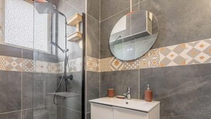 Um banheiro com chuveiro em box de vidro, pia branca com espelho e azulejos estampados.
