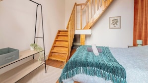 Quarto com escada de madeira, cama com manta azul-turquesa, mesa de cabeceira e uma planta.