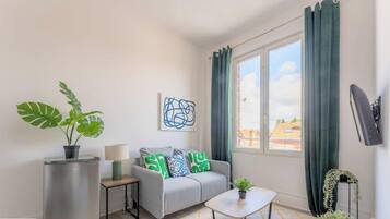Ein modernes Wohnzimmer mit grauem Sofa, einem kleinen Tisch, einem Blumentopf und einem Fenster mit Vorhängen.