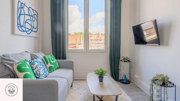 Sala de estar com sofá, mesa de centro, televisão e janela com cortinas.