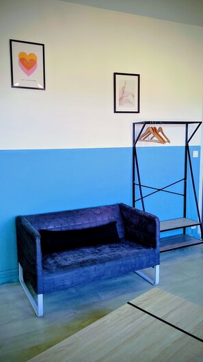 Quarto com um sofá azul, um porta-roupas fixado na parede e duas imagens emolduradas.