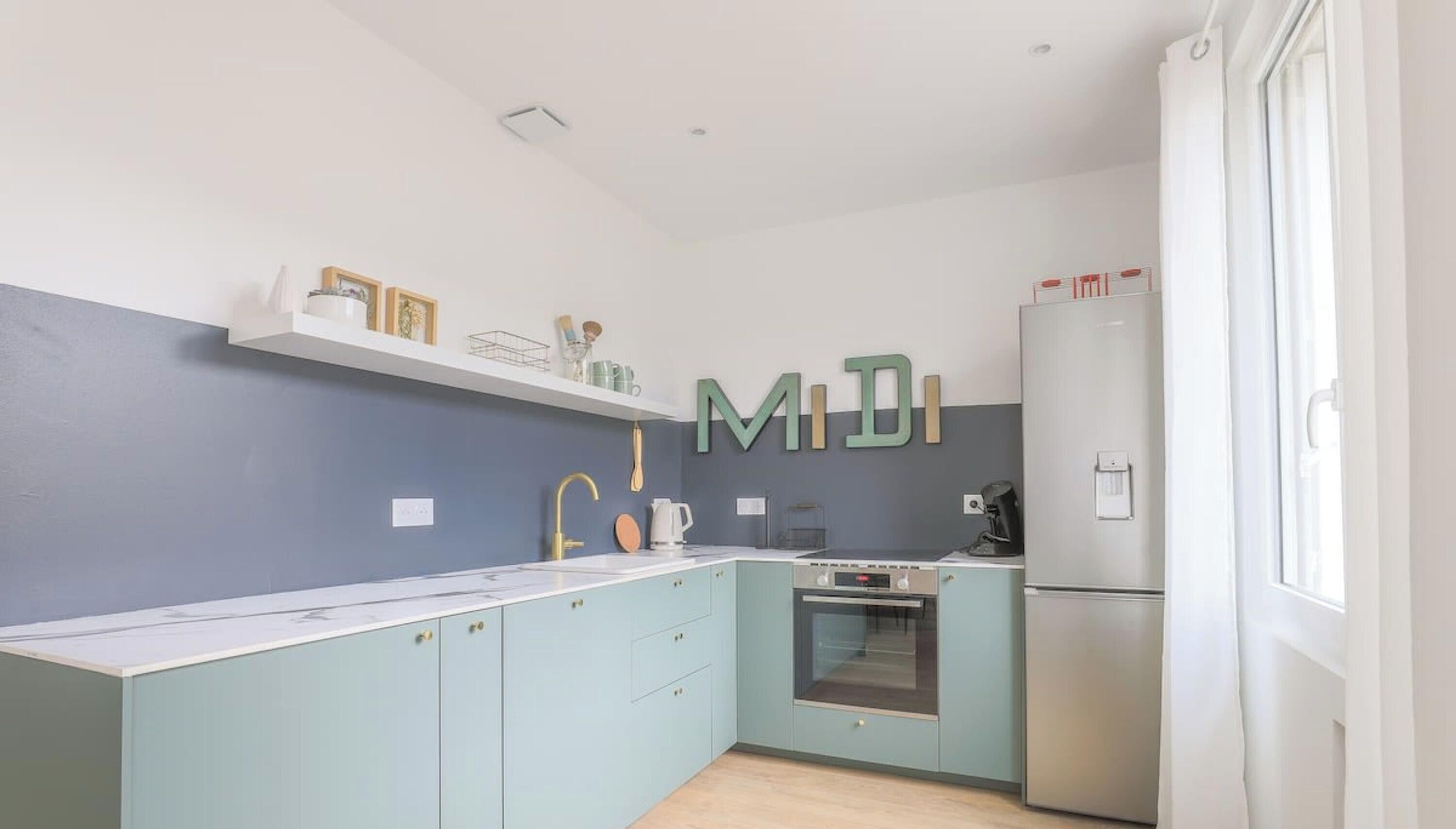 Una cocina moderna con armarios azul claro, una encimera blanca, horno empotrado y refrigerador.