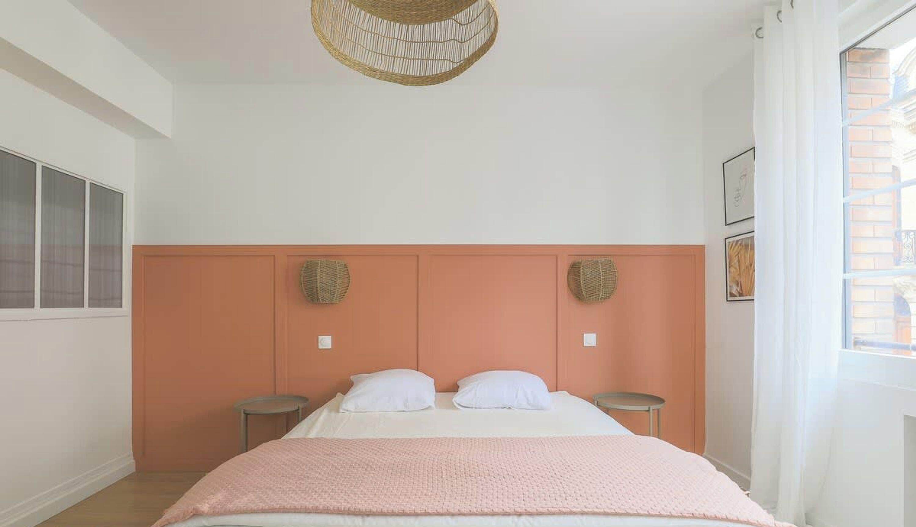 A bedroom with a bed, two bedside tables, a hanging light fixture, and a window with curtains.
