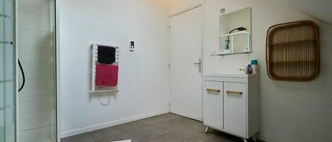 A bathroom with a shower, a white cabinet with drawers, a mirror, and a towel rack.