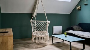 Een kamer met een hangstoel, een bank, een salontafel, een radiator en een dakraam.