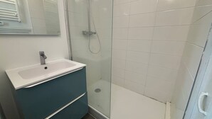 A bathroom with a white sink, a mirror, a shower enclosure, and a tiled floor. - Le Rietz 3 T2 Proche Gare et Parc (Arras)