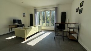 A living room with a sofa, a TV, a desk, and a window with curtains. - Le Rietz 3 T2 Proche Gare et Parc (Arras)