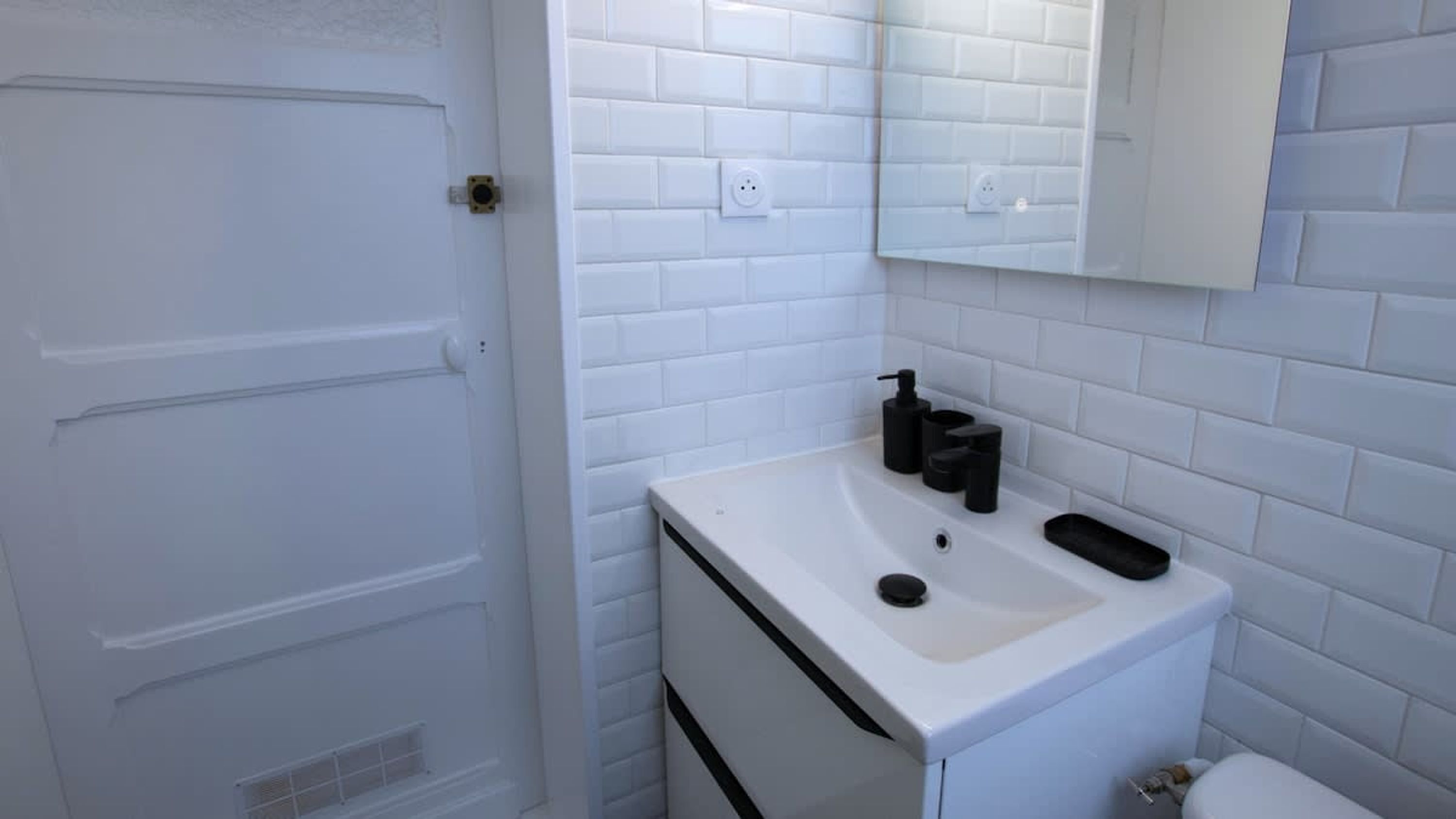 A bathroom with white subway tiles, a white sink with black soap dispensers, and a mirror above the sink.