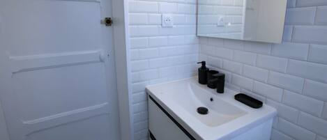 A bathroom with white subway tiles, a white sink with black soap dispensers, and a mirror above the sink.