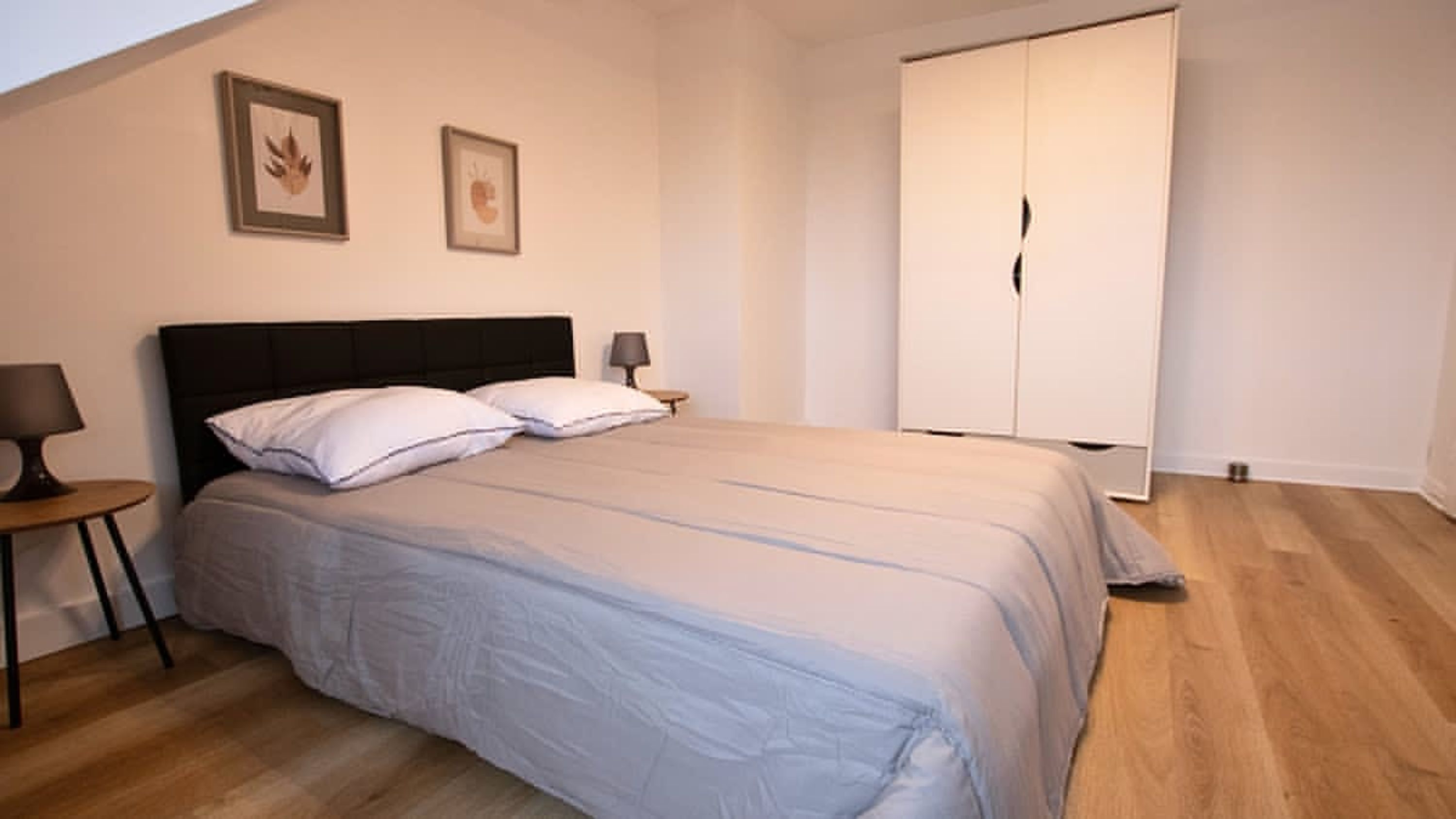 Een slaapkamer met een bed, twee nachtkastjes, een garderobe en twee ingelijste foto’s aan de muur.