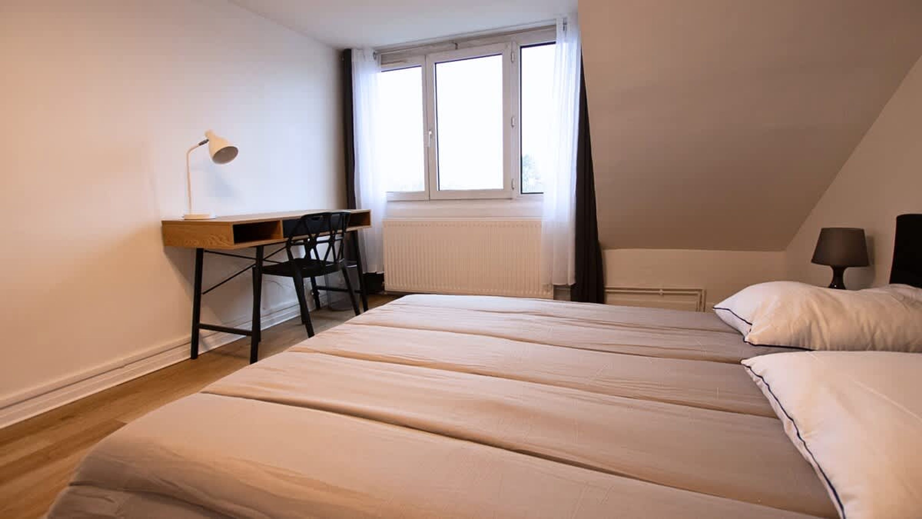 Quarto com cama, escrivaninha, cadeira, janela e radiador.