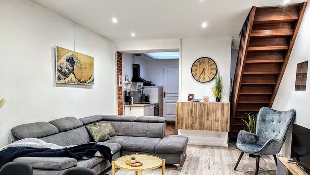 A modern living room with a sectional sofa, a round coffee table, a grey armchair, and a wooden staircase.