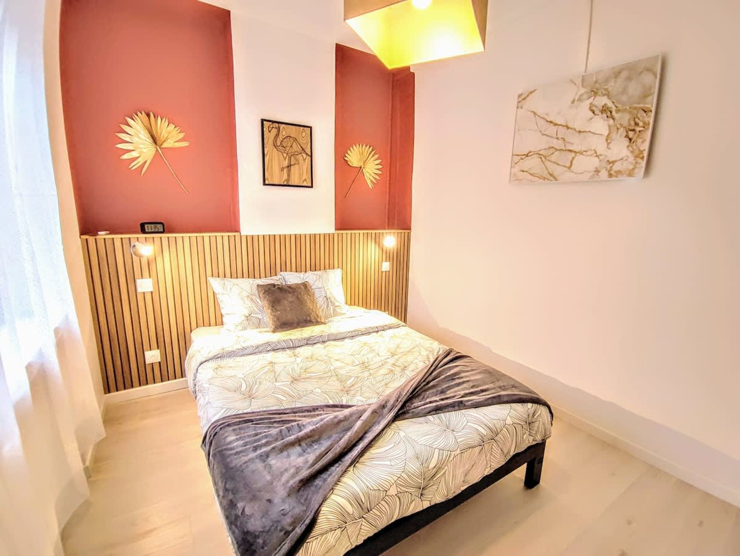 A bedroom with a bed, wooden headboard, wall art, and a light fixture.