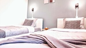 A hotel room with two beds, a nightstand, a lamp, and a wall-mounted shelf.