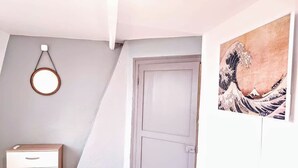 A room with a white door, a wooden dresser with drawers, a round mirror on the wall, and a Japanese wave painting.
