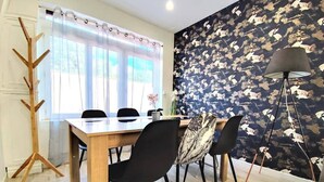 A dining area with a wooden table, black chairs, a wooden coat rack, and a wall with a bird pattern.