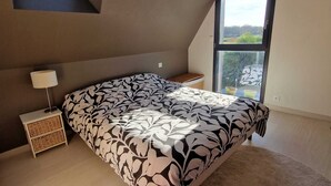 A bedroom with a large bed, a nightstand, a lamp, a window with a view, and a sloped ceiling. - La maison aux palmiers, swimming pool, spa (Sorigny)