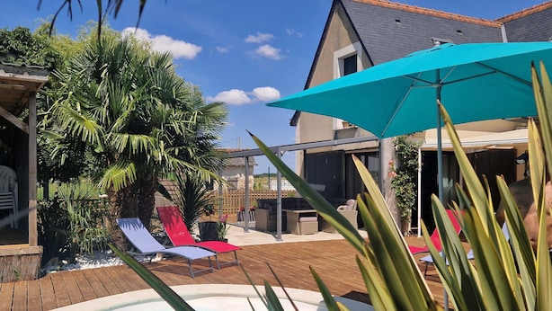 A swimming pool with lounge chairs, a patio area, and a house in the background. - La maison aux palmiers, swimming pool, spa (Sorigny)