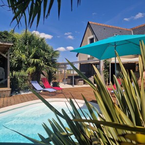 Une piscine avec des chaises longues, un espace patio et une maison en arrière-plan.