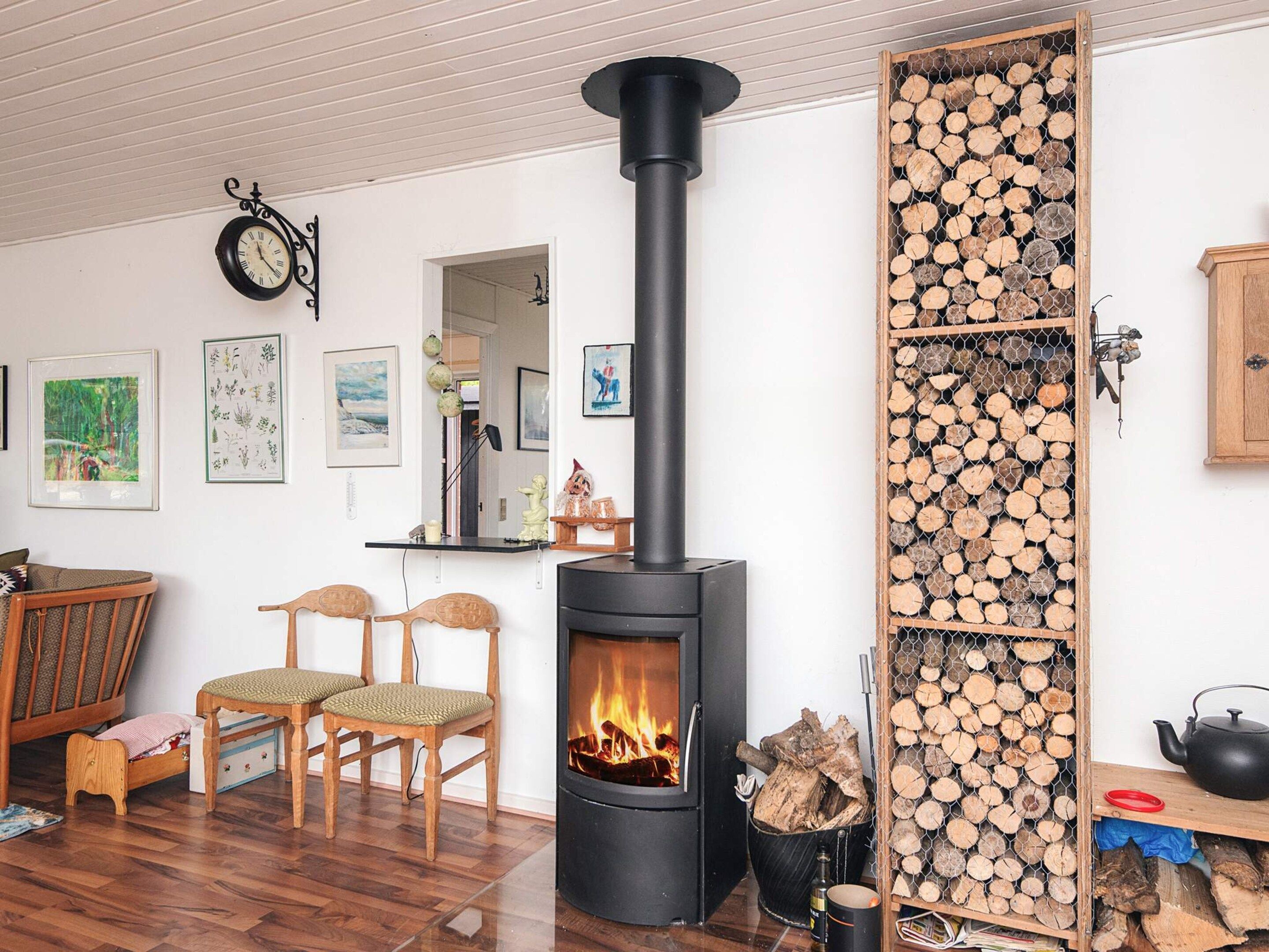 Ein gemütliches Zimmer mit Kaminofen, einer Uhr und einem Holzstoß an der Wand.