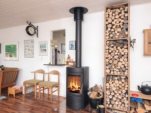 Een knus ingerichte kamer met een houtkachel, een klok en een wandplank met diverse spullen.
