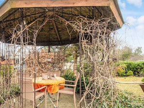 A gazebo with a round table and chairs, surrounded by a metal fence and overgrown with vines. - 4 Person Holiday Home in Norre Nebel (Norre Nebel)