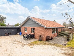A small brick house with a tiled roof, a patio with outdoor furniture, and a fenced yard. - 4 Person Holiday Home in Norre Nebel (Norre Nebel)