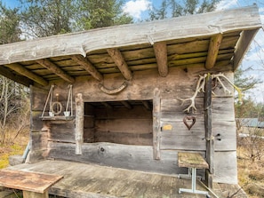 A rustic wooden structure with a slanted roof, a small bench, and a hanging light fixture. - 4 Person Holiday Home in Norre Nebel (Norre Nebel)