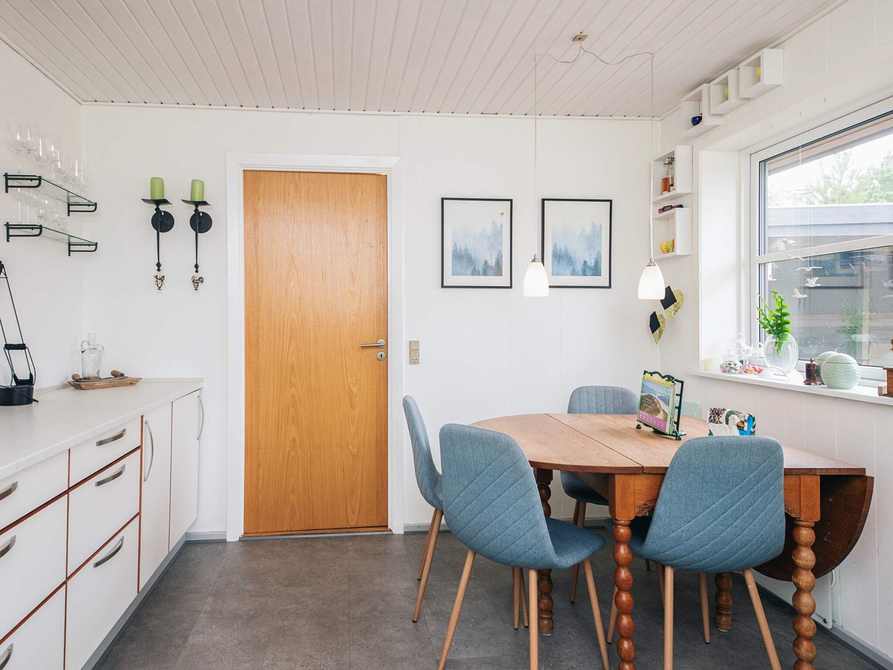 Un comedor con una mesa de madera, dos sillas azules, un armario blanco y una ventana con vistas.