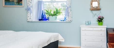A bedroom with a bed, a dresser, a window with curtains, a clock, a painting, and a potted plant.