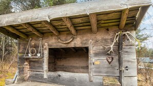 Una struttura in legno rustica con tetto spiovente, una piccola panchina e un lampadario a sospensione.