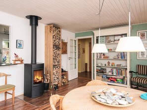 A cozy living room with a fireplace, wooden bookshelf, and a dining table with a bowl of snacks. - 4 Person Holiday Home in Norre Nebel (Norre Nebel)