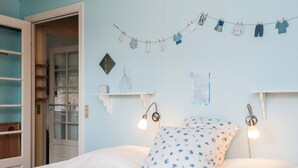 Una camera da letto con un letto, due lampade da comodino, uno scaffale a parete e un filo steso con vestiti da bambini.