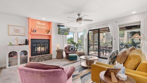 Una sala de estar con chimenea, un sofá, una silla, un televisor y un balcón con mobiliario exterior.